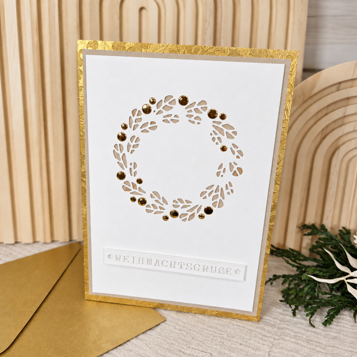Vorderseite der Weihnachtskarte in Gold und Weiß mit ausgestanztem Blätterkranz und goldfarbenen Verzierungen