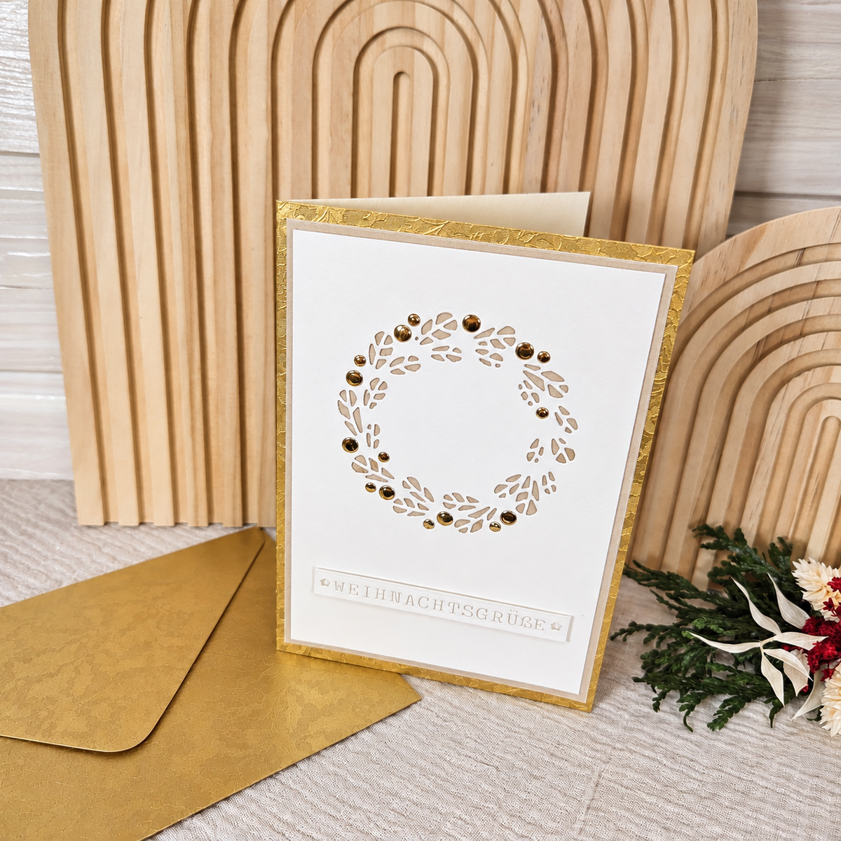 Weihnachtskarte „Weihnachtsgrüße“ mit goldfarbenem Umschlag vor einem hellen Holzhintergrund