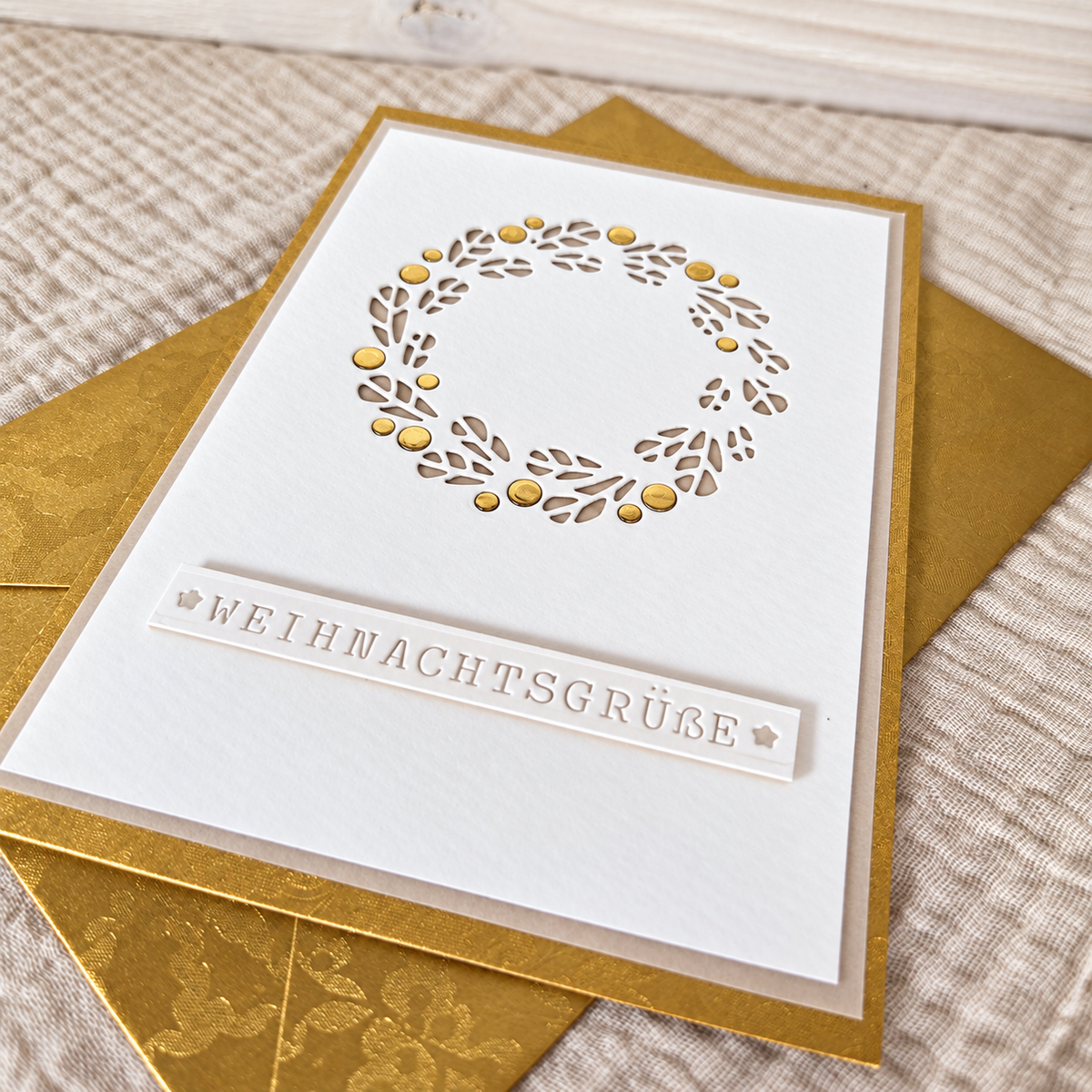 Weihnachtskarte in Gold und Weiß auf einem goldfarbenen Umschlag liegend