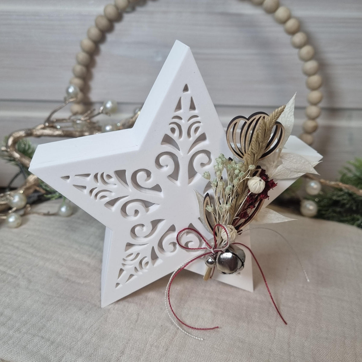 Weißer Gießkeramikstern mit Trockenblumenarrangement und kleinem Glöckchen