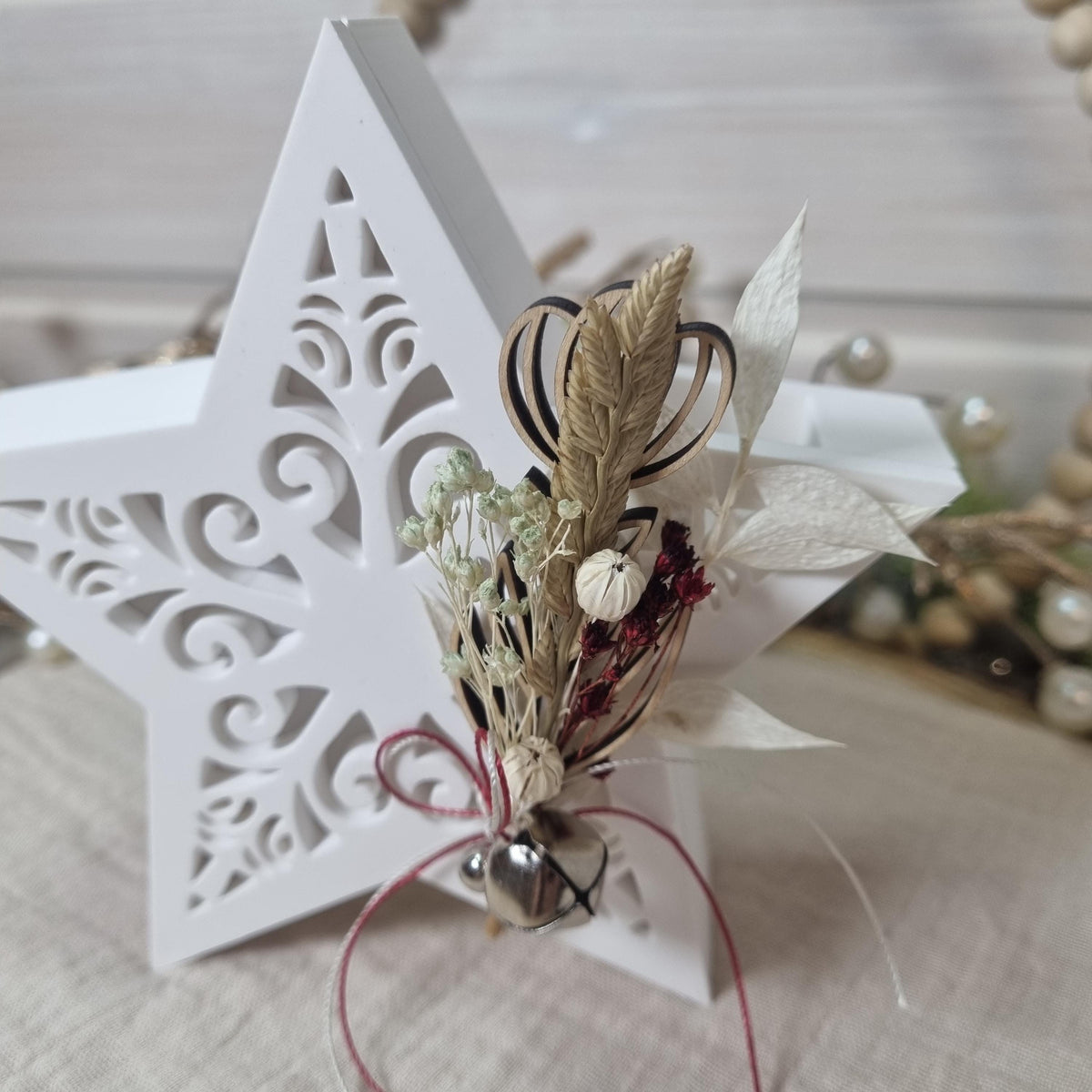 Weißer Gießkeramikstern mit Trockenblumenarrangement und kleinem Glöckchen