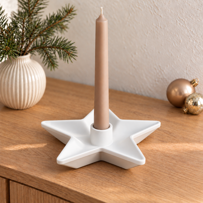 Weißer Sternkerzenhalter mit beigefarbener Stabkerze auf einer Holzkommode neben einer Vase mit Tannenzweigen.